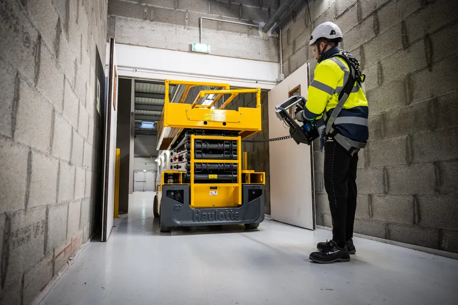 Operador conduzindo plataforma tesoura Haulotte por porta estreita