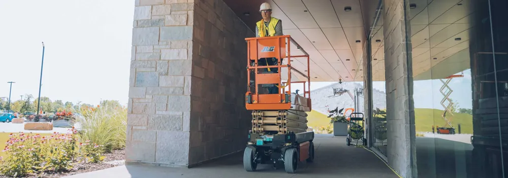 Plataforma tesoura elétrica JLG em área externa sob marquise